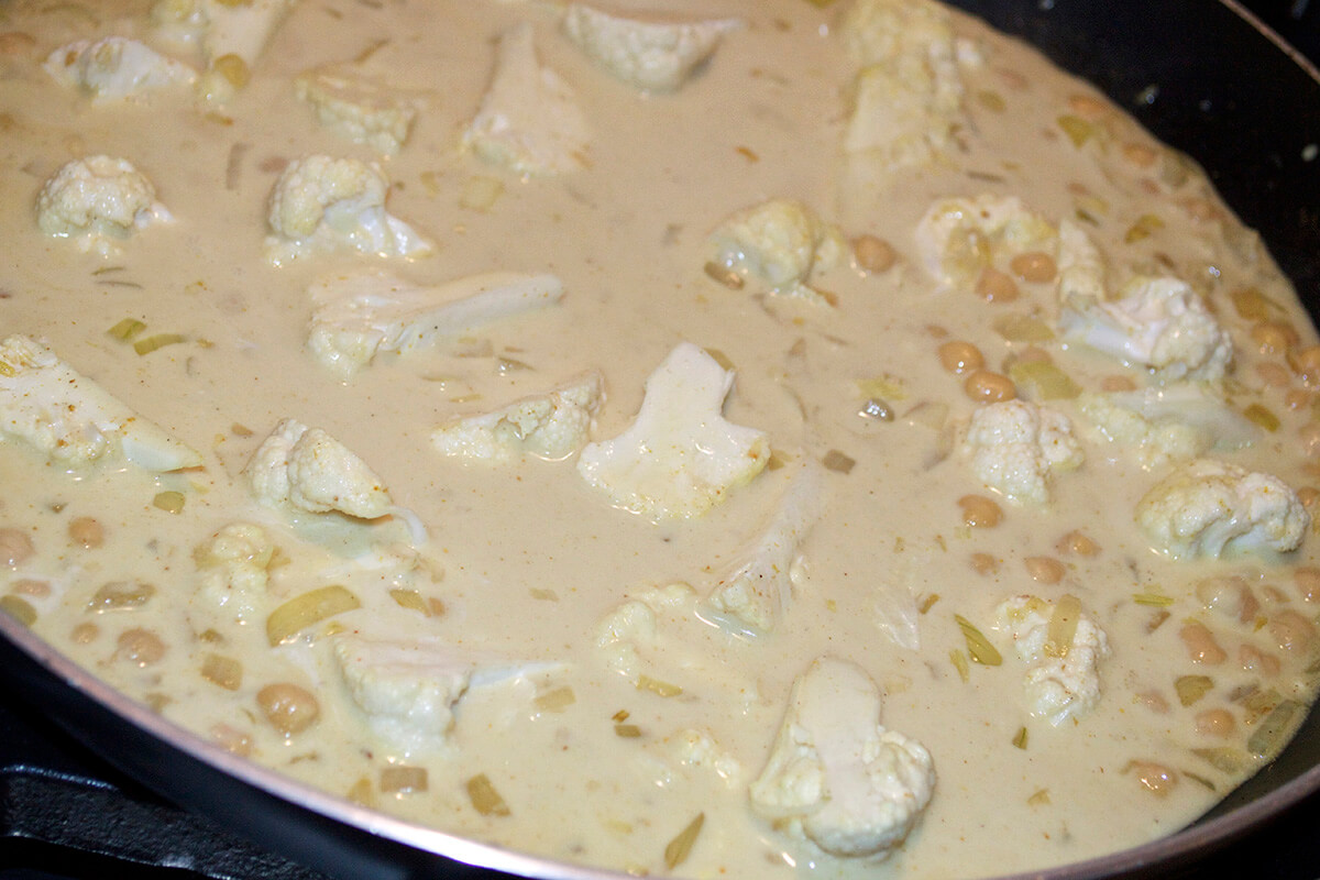 A saucepan with onion, garlic, chickpeas and cauliflower in stock and coconut milk