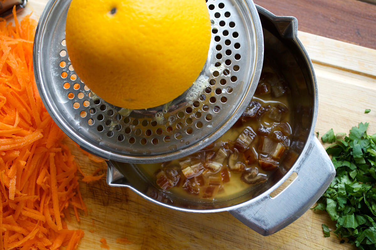 A chopping board with dates being softened in orange juice next to grated carrot and chopped coriander