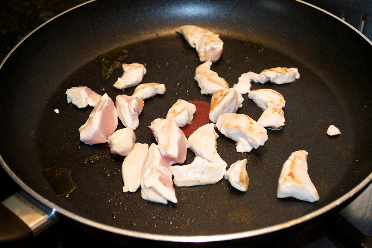 Diced chicken being cooked in frying pan