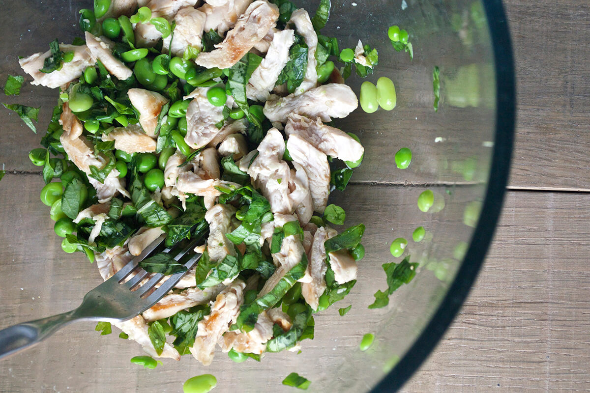 A bowl of cooked chicken, broad beans, peas and basil