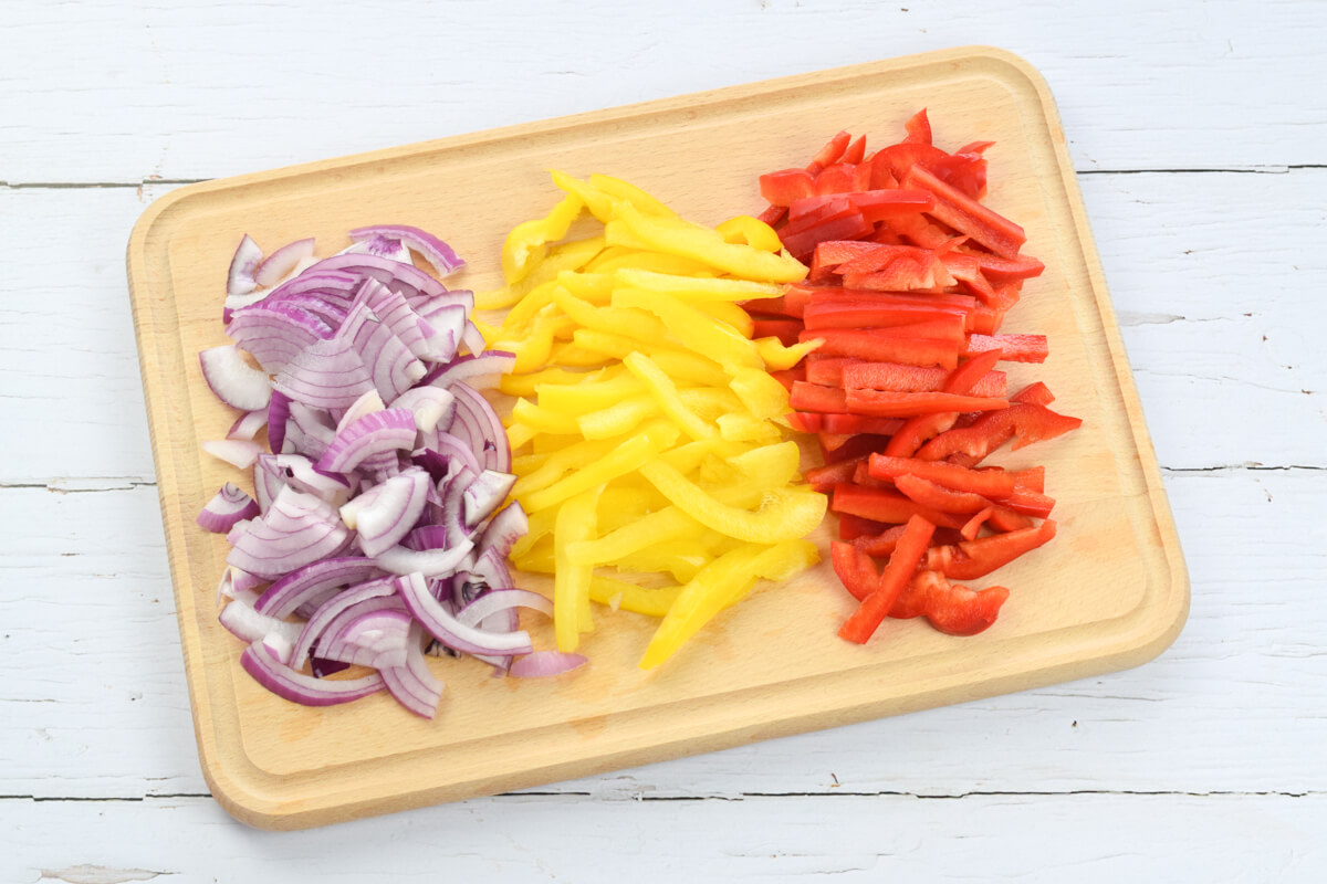 A chopping board with sliced red onion, yellow and red pepeprs