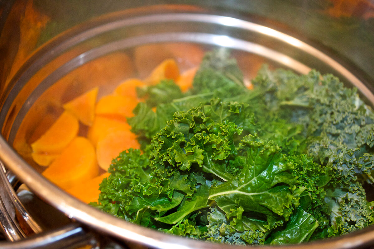A saucepan of sweet potato and kale being steamed