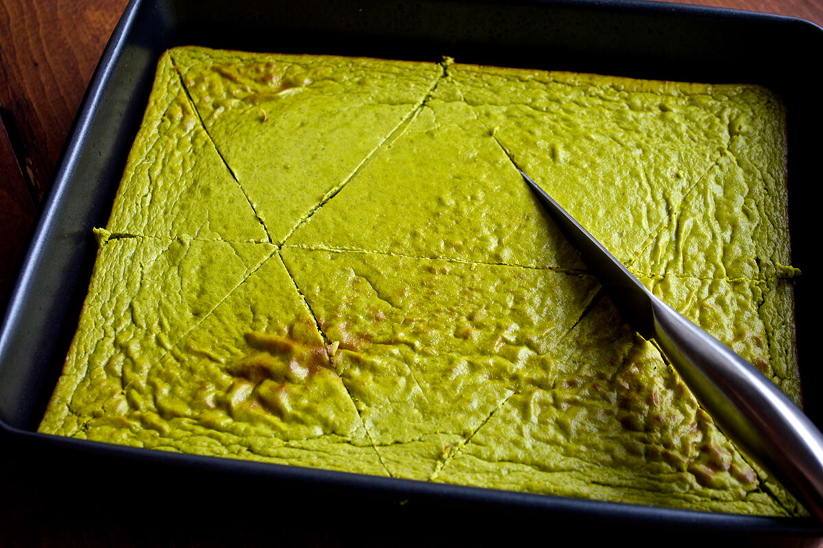 A rectangular baking tin with green tart mixture in it being cut into triangles