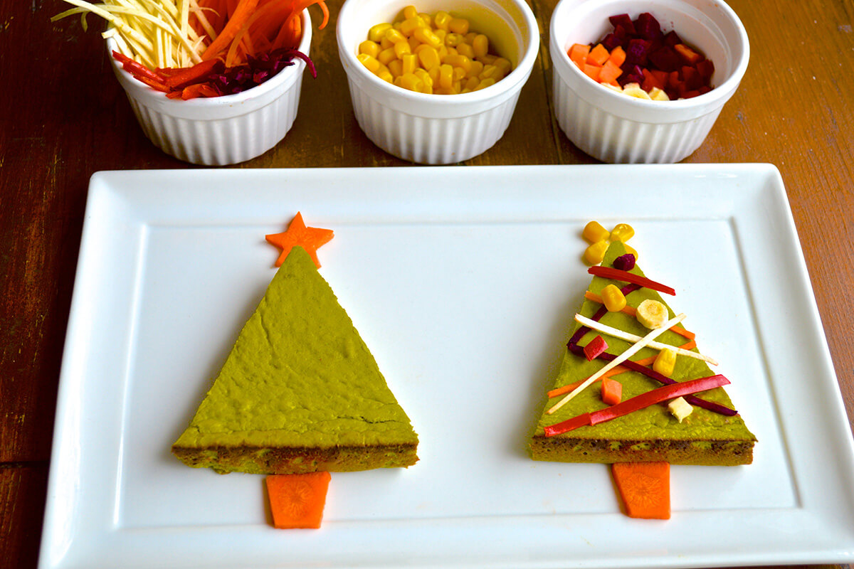 Christmas Tree tarts cut into triangles and decorated to look like trees, next to bowls of shredded and cut vegetables