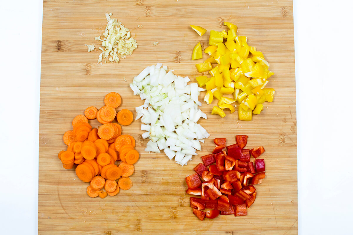 A chopping board with chopped onion, carrot, pepper and crushed garlic