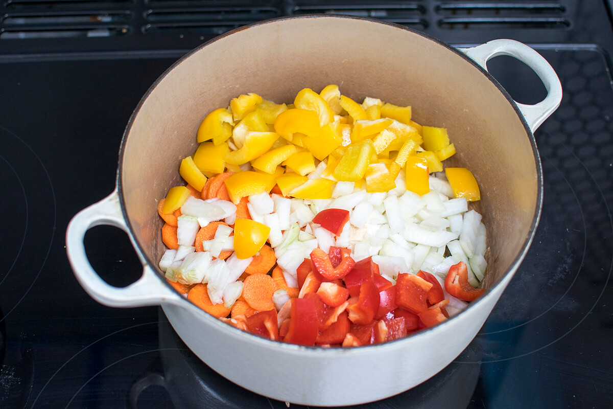 A saucepan with chopped onion, carrot, pepper and crushed garlic