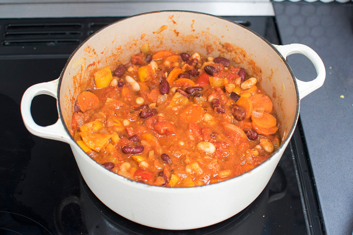 A saucepan with chopped onion, carrot, pepper and crushed garlic, red kidney and cannellini beans and plum tomatoes