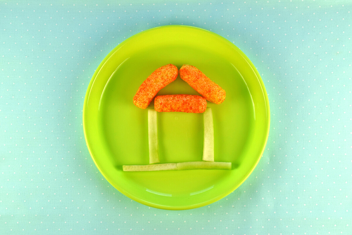 3 carrot puffs places above the vertical cucumber sticks in a triangle to create a house roof