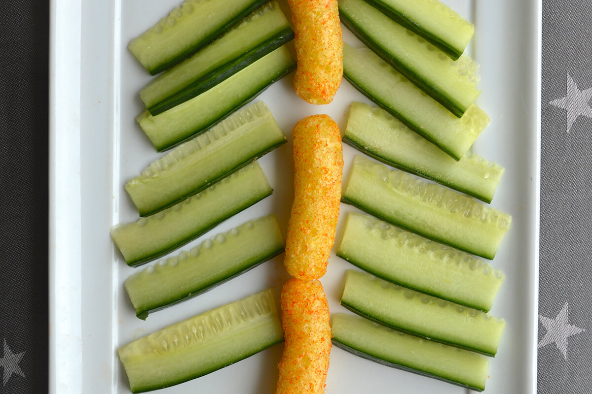 3 carrot puffs placed in centre of large plate to create tree trunk. Cucumber batons  placed on plate to create Christmas tree branches