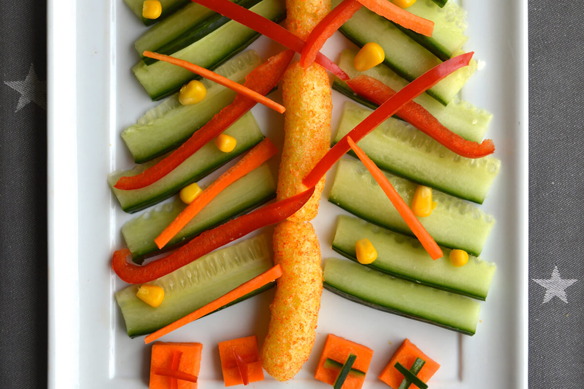 Carrot squares placed under tree with pepper and cucumber strips on top to create present boxes with ribbons