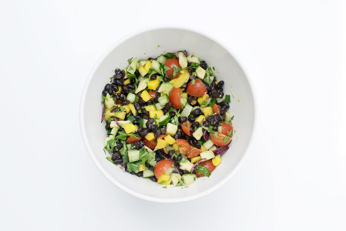 A bowl of mango salsa: mango, cucumber, avocado, cherry tomatoes, red onion, fresh coriander and black beans with lime juice