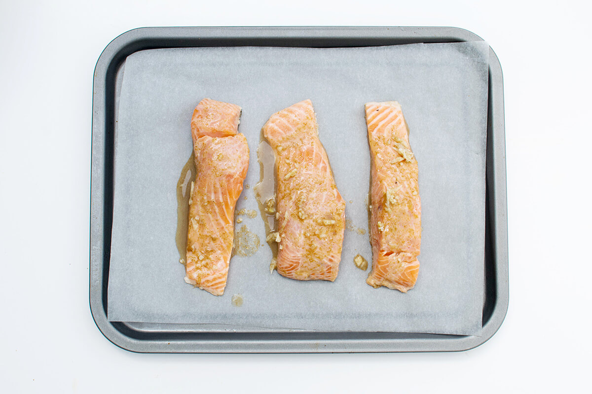 A baking tray lined with parchment paper, with three baked salmon fillets on it