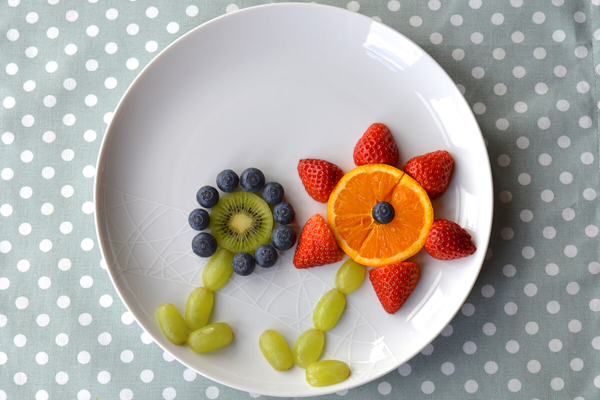 Blueberry halves placed around the kiwi and halved strawberry around the orange to create petals