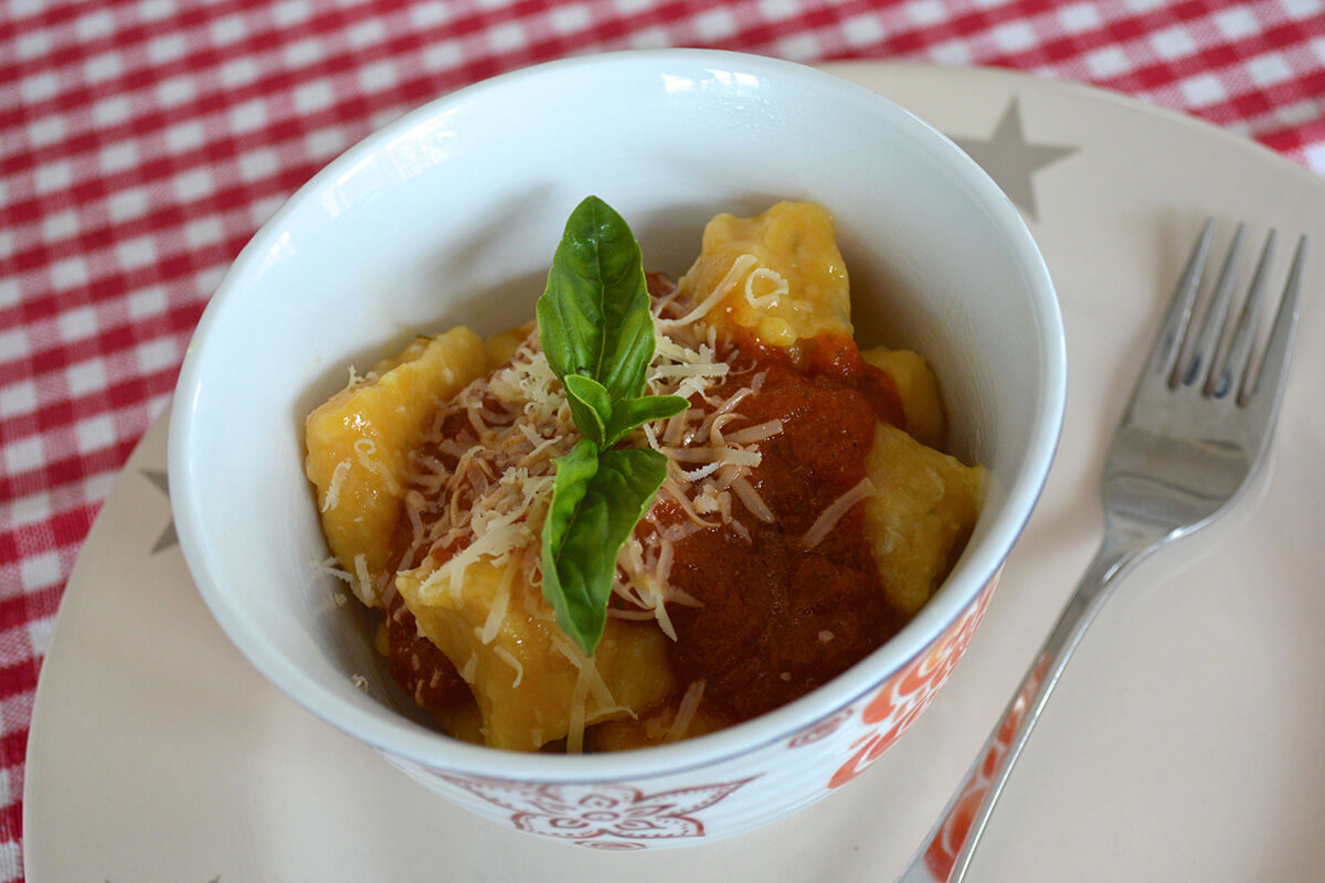 A bowl of Gnocchi With Tomato & Basil topped with cheese and fresh basil leaves