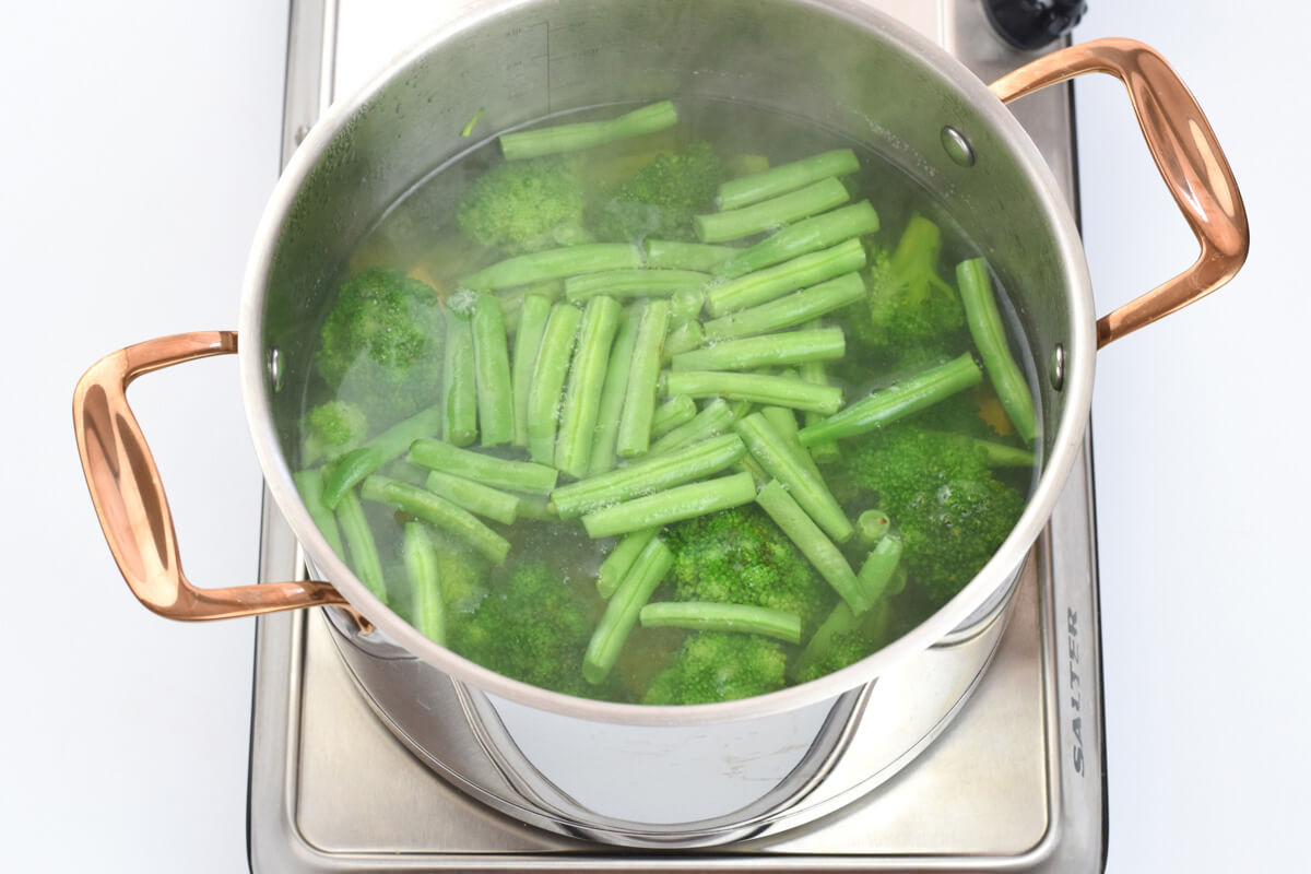 A saucepan of green beans and broccoli being cooked in water