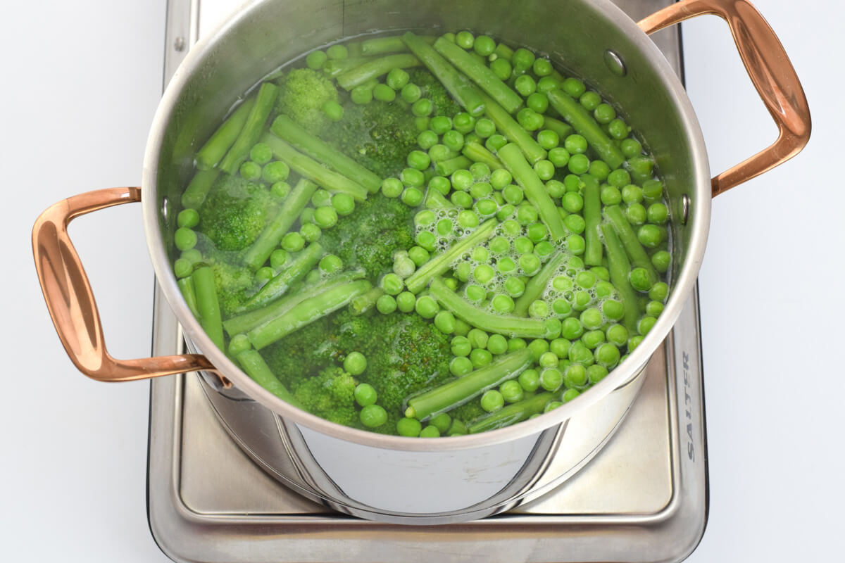 A saucepan of green beans, broccoli and peas being cooked in water