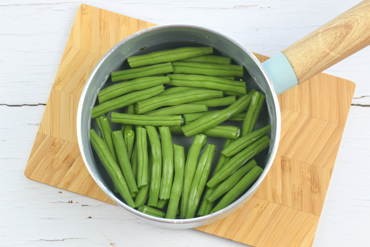 A wooden chopping board with a saucepan of chopped green beans in water