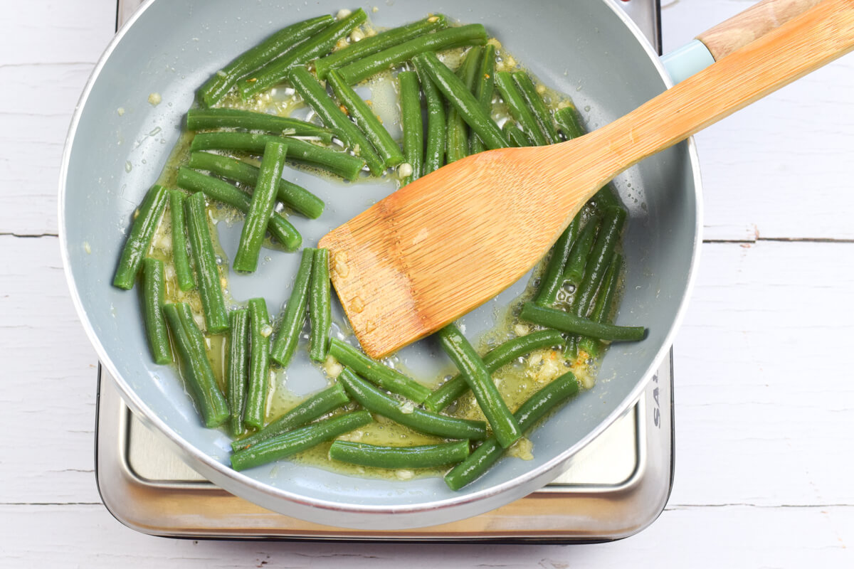 A frying pan with chopped green beans being fried in garlicky butter