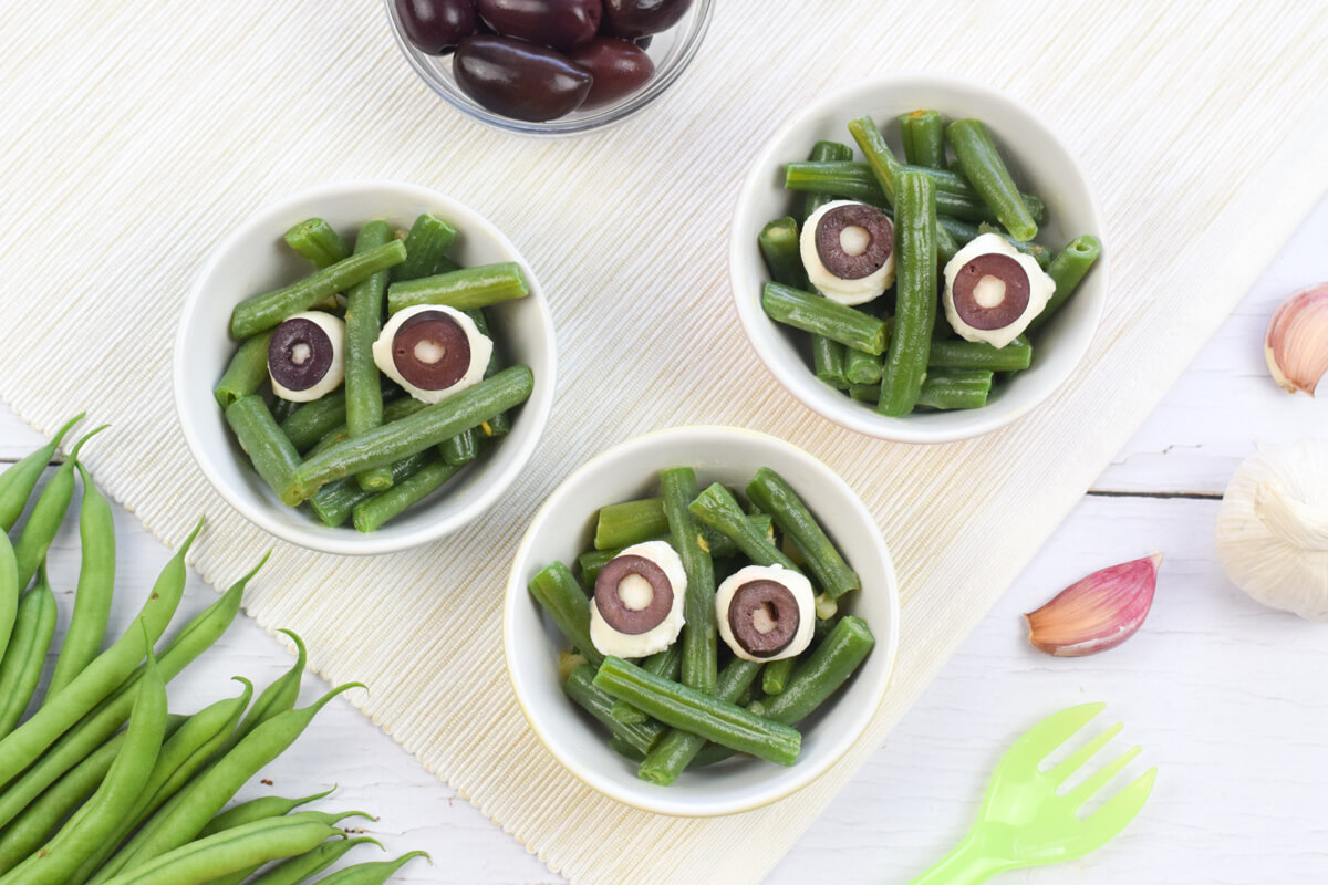 3 small bowls of green bean monsters: green beans topped with small mozzarella bowls and sliced black olives to create eyes