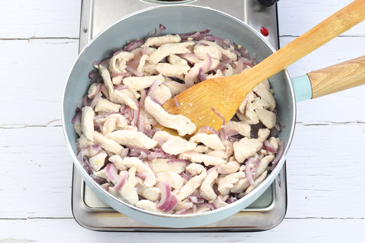 A frying pan with chicken and red onion being fried together
