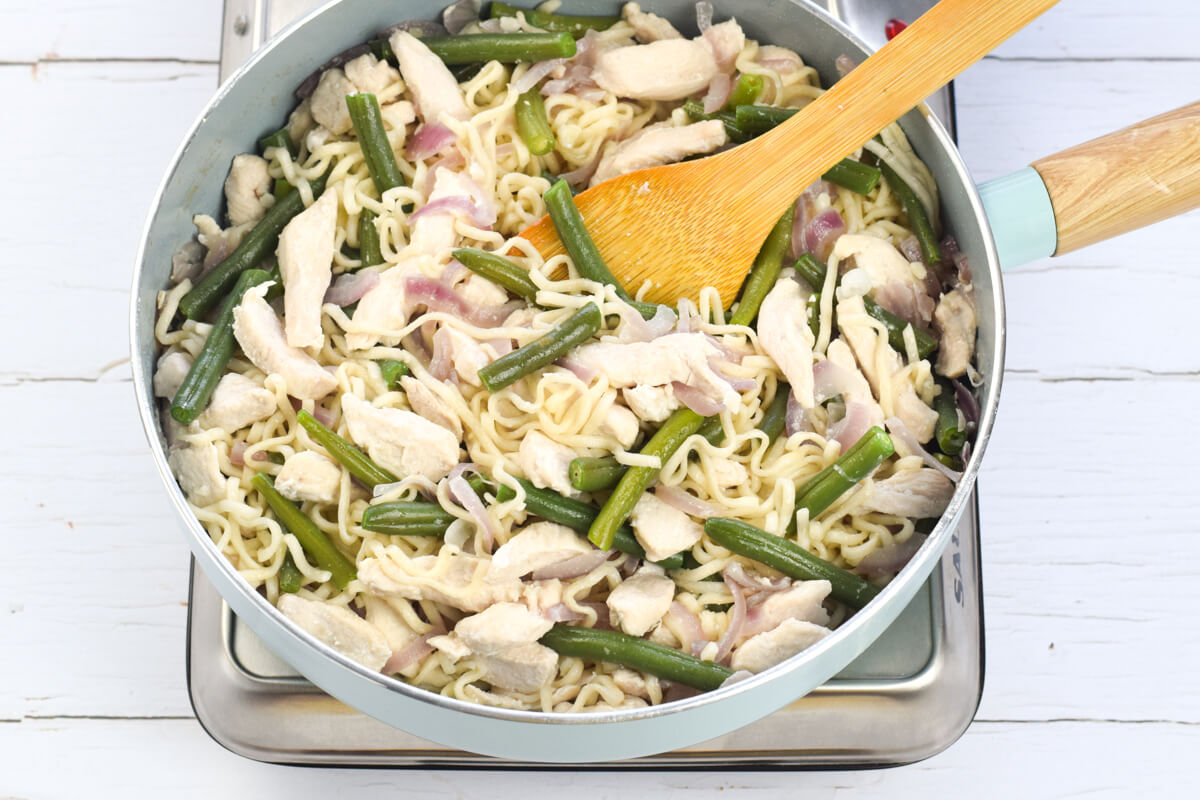 A frying pan with chicken and red onion being fried together wit green beans and noodles