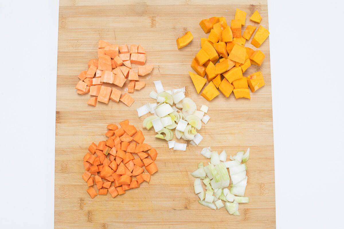 A wooden chopping board with diced pumpkin, carrots, onion, leek and sweet potato