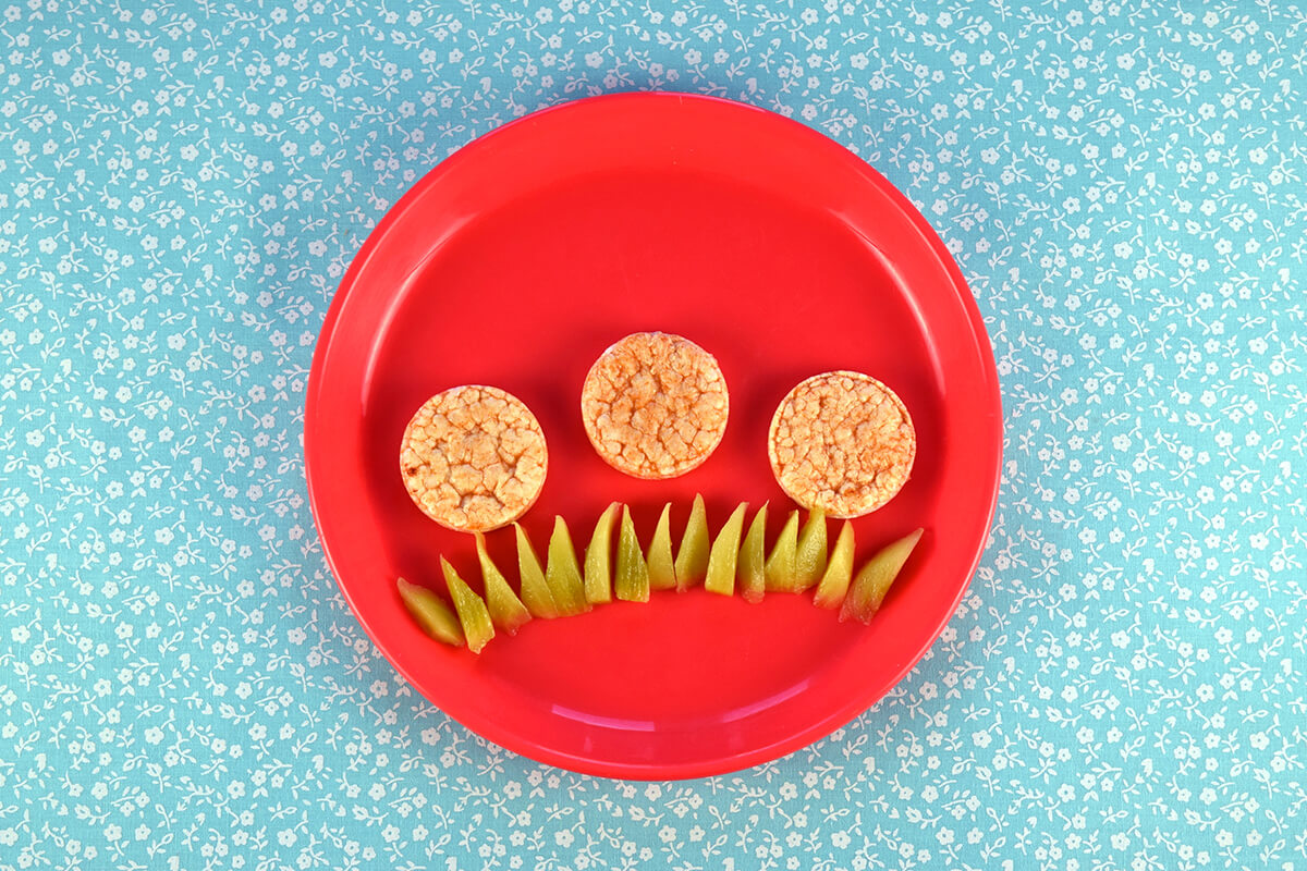 Sliced kiwi pieces arranged on bottom of plate to create grass. Three mini rice cakes are arranged above the kiwi grass