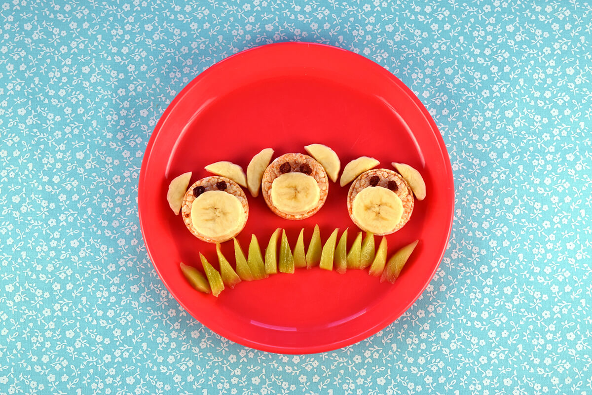 Halved raisins are placed in centre of rice cakes above the bananas, to create eyes