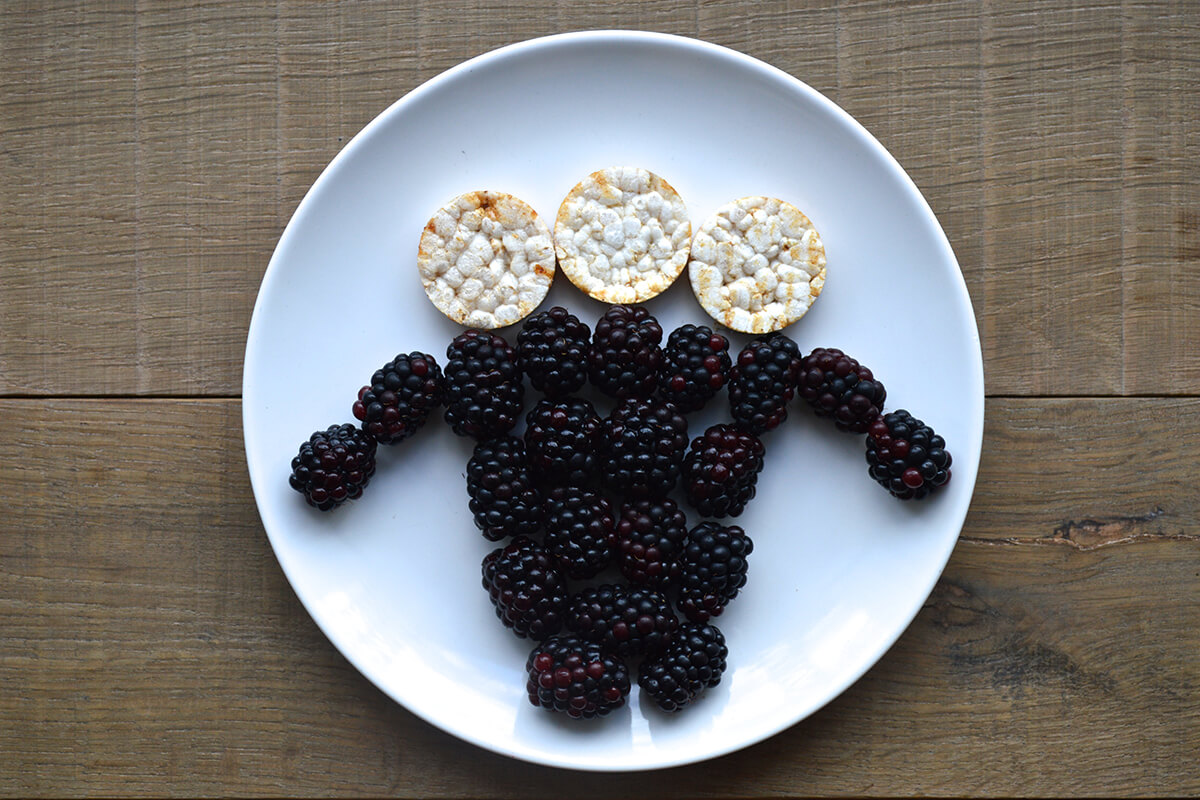 Three apple rice cakes arranged above blackberries to create a woolly sheep head