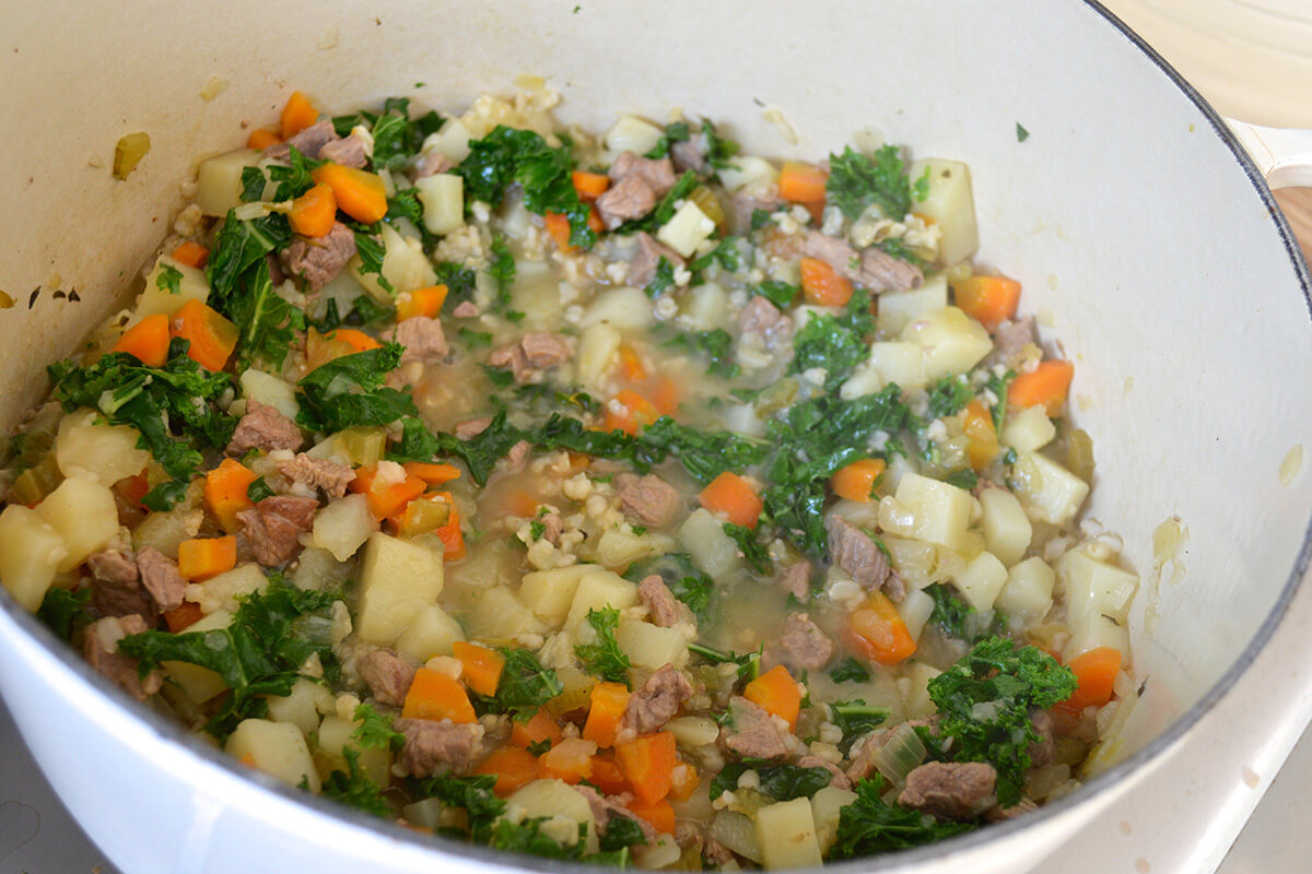 Lamb in a saucepan with onion, celery, herbs and stock, carrots and potatoes