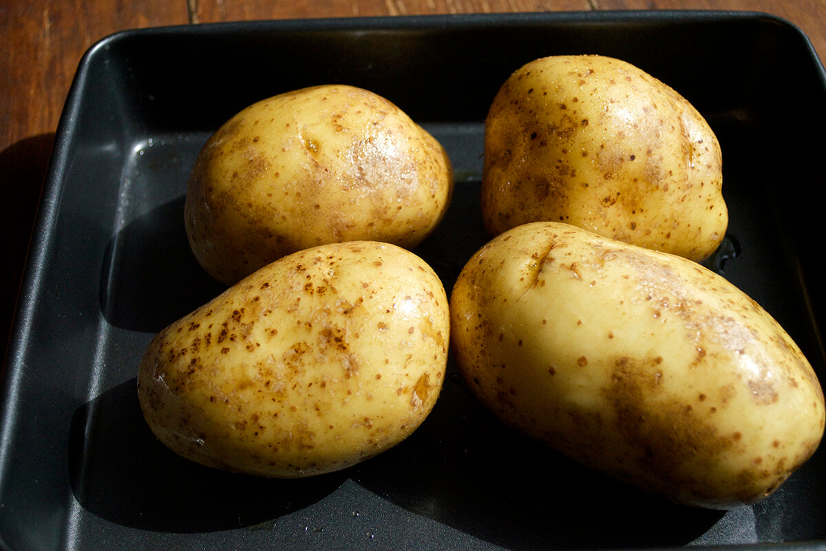 Four raw potatoes on a baking tray