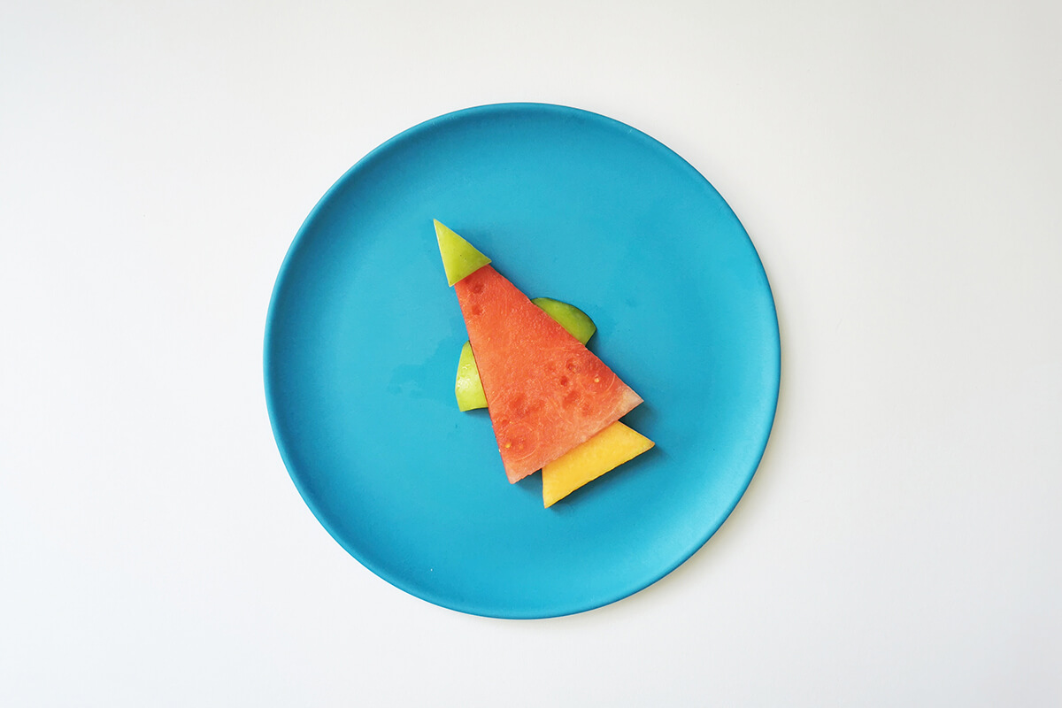 Watermelon triangle placed on plate with two apple fingers on either side, apple triangle on top and cantaloupe slice at the bottom of the triangle rocket shape