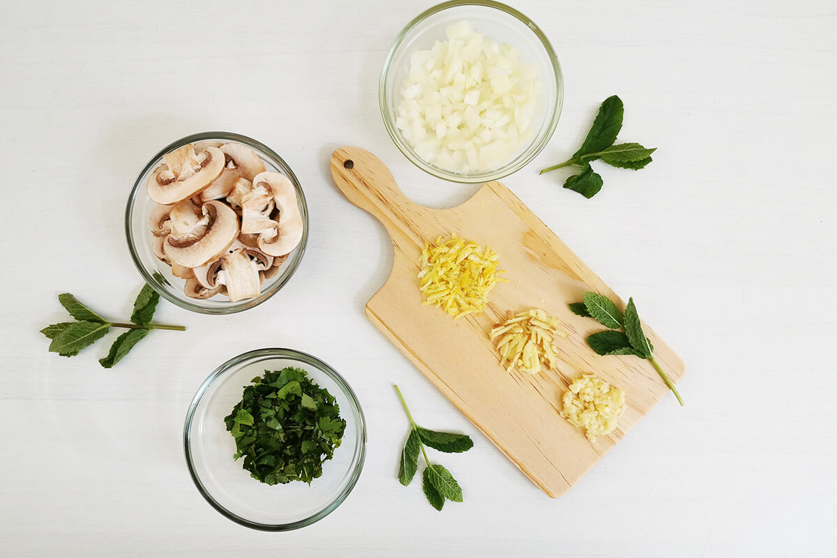 A chopping board with lamb kofta ingredients next to a bowl of mushroom, chopped onion and coriander