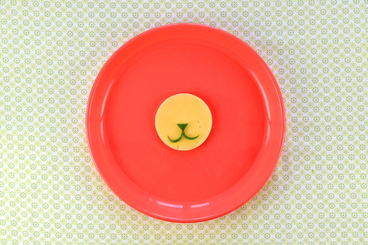 Cheese circle placed on centre of plate with cucumber triangle and have moons placed to create a lion nose and mouth