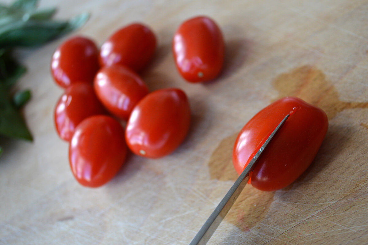 A chopping board with cherry tomatoes being sliced