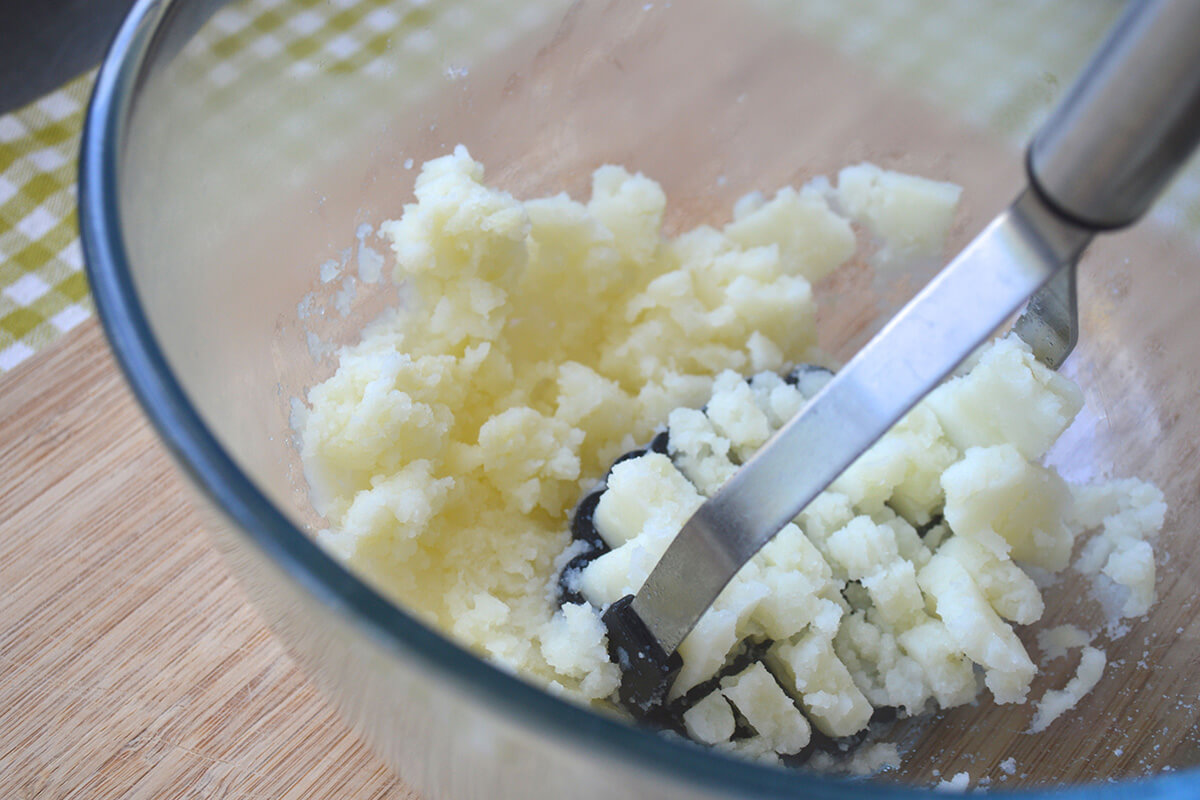 Potato being mashed in a large glass bowl