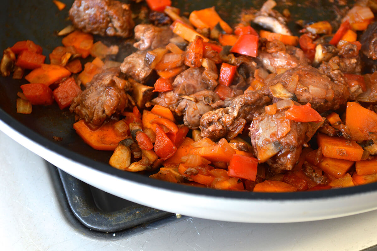 A pan of onions, pepper, carrots and mushrooms being fried with tomato puree and liver