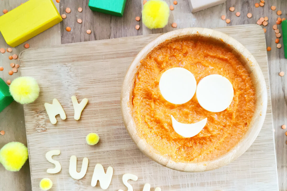 Half a jar of Organix butternut squash, tomato, lentil & olive oil is placed into a bowl with two circular slices of cheese for eyes and a half moon cheese shape for a mouth