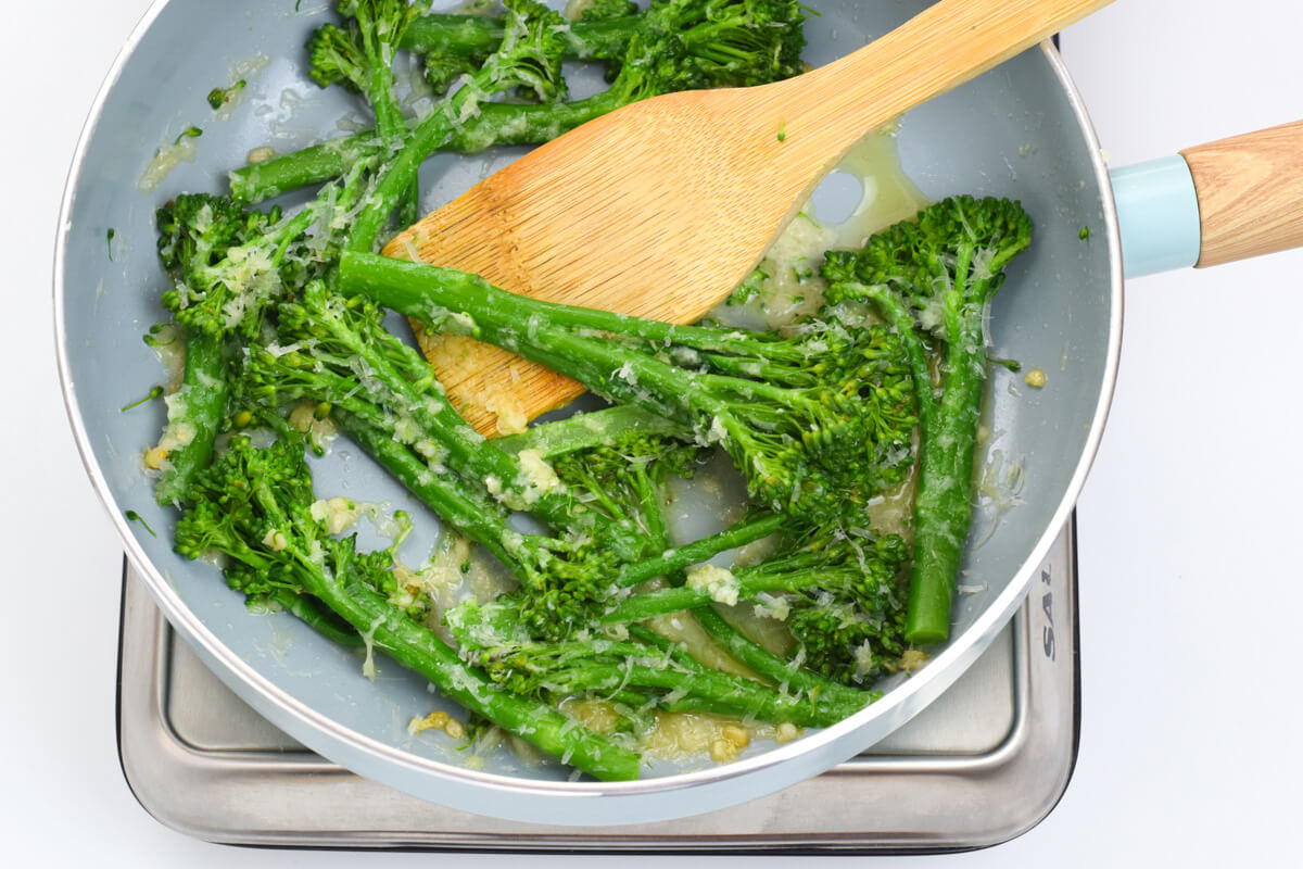 A pan of tenderstem broccoli being coated in garlicky butter and parmesan