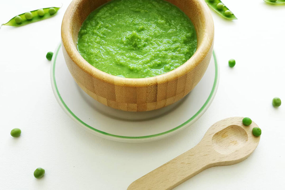 Pea puree in a small bowl with some peas around it