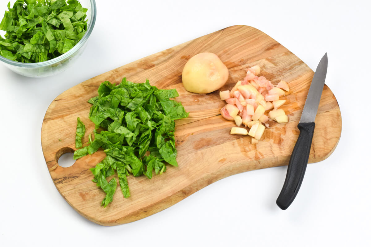 A chopping board with copped spinach leaves and diced peach, next to a small glass bowl of chopped spinach leaves
