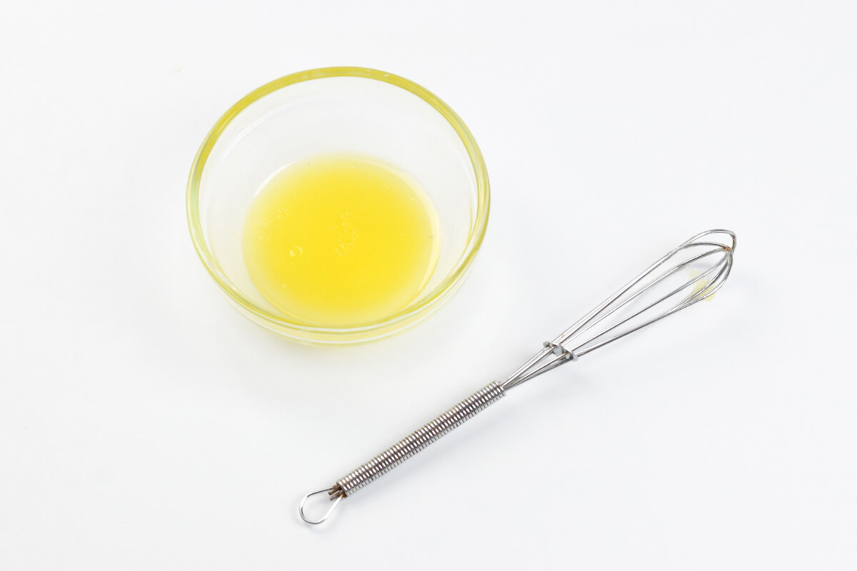 A glass bowl with salad dressing, next to a whisk
