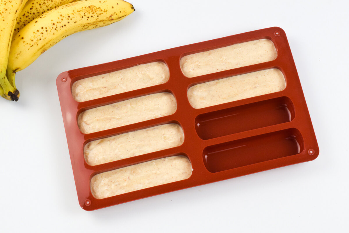 Peanut butter-banana mix in a silicone mould, next to 2 ripe bananas