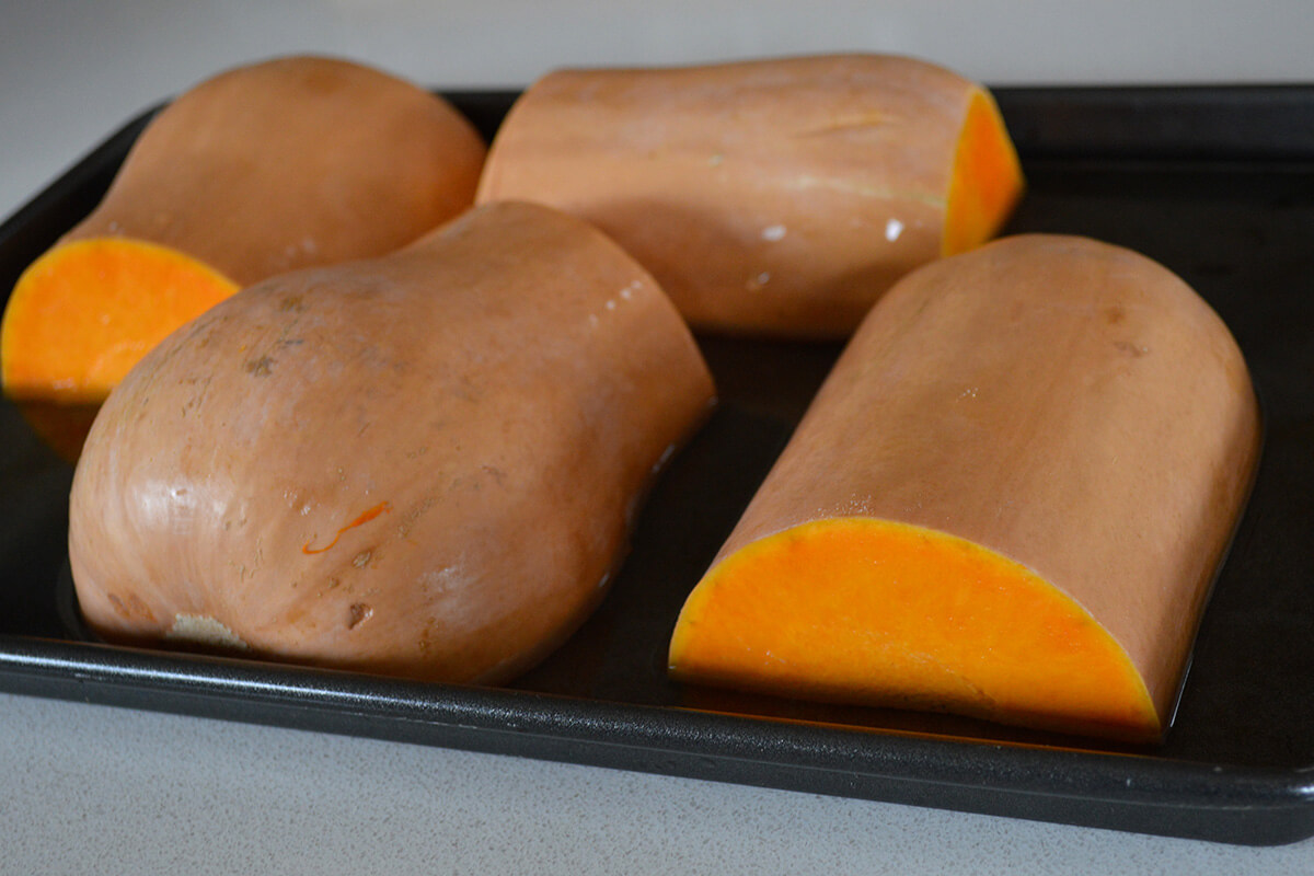 Two halved butternut squash on a roasting tray