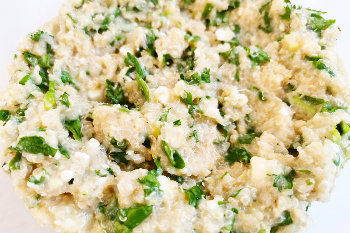 A bowl of quinoa combined with chopped spring onion, spinach, watercress, herbs, cheese and eggs