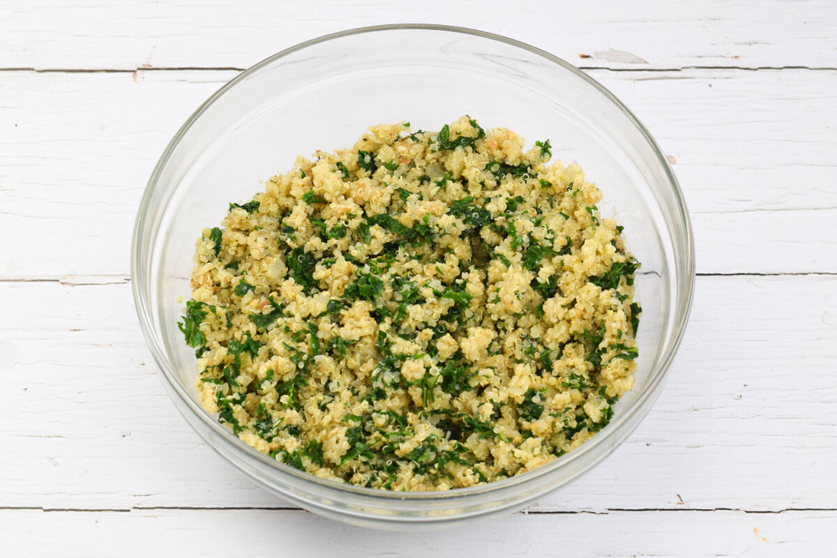 A glass bowl with kale, quinoa, onion, garlic, whisked egg and parmesan, breadcrumbs and herbs