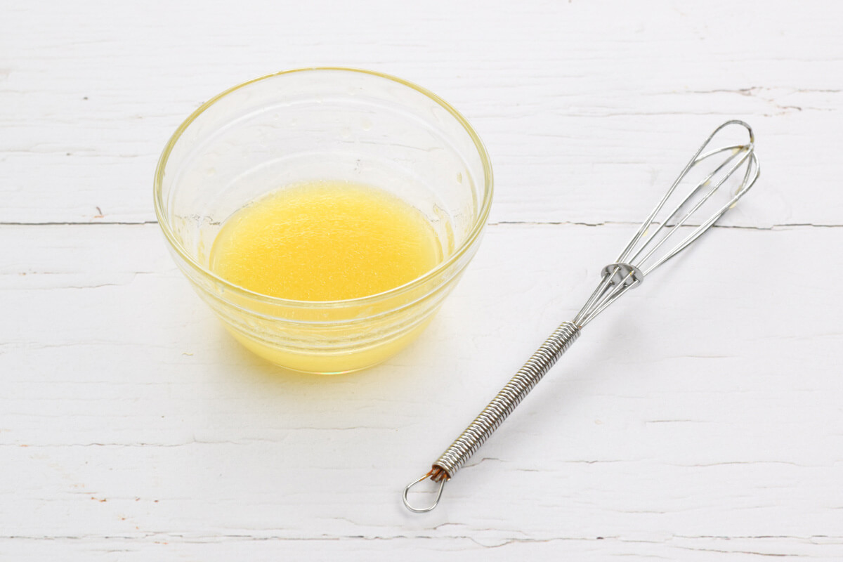 A small glass bowl of salad dressing next to a whisk