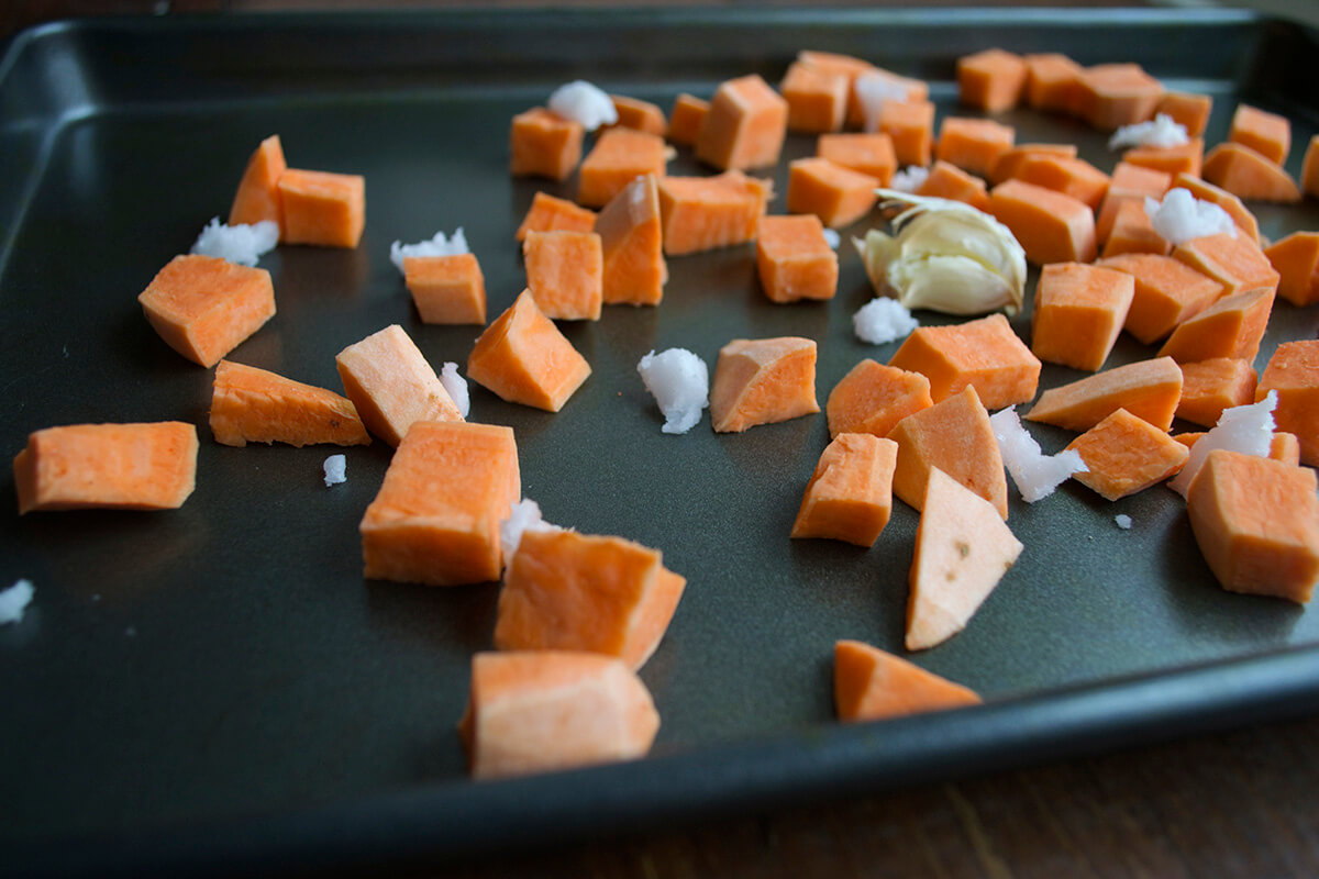 Diced raw sweet potato and garlic on a roasting tray
