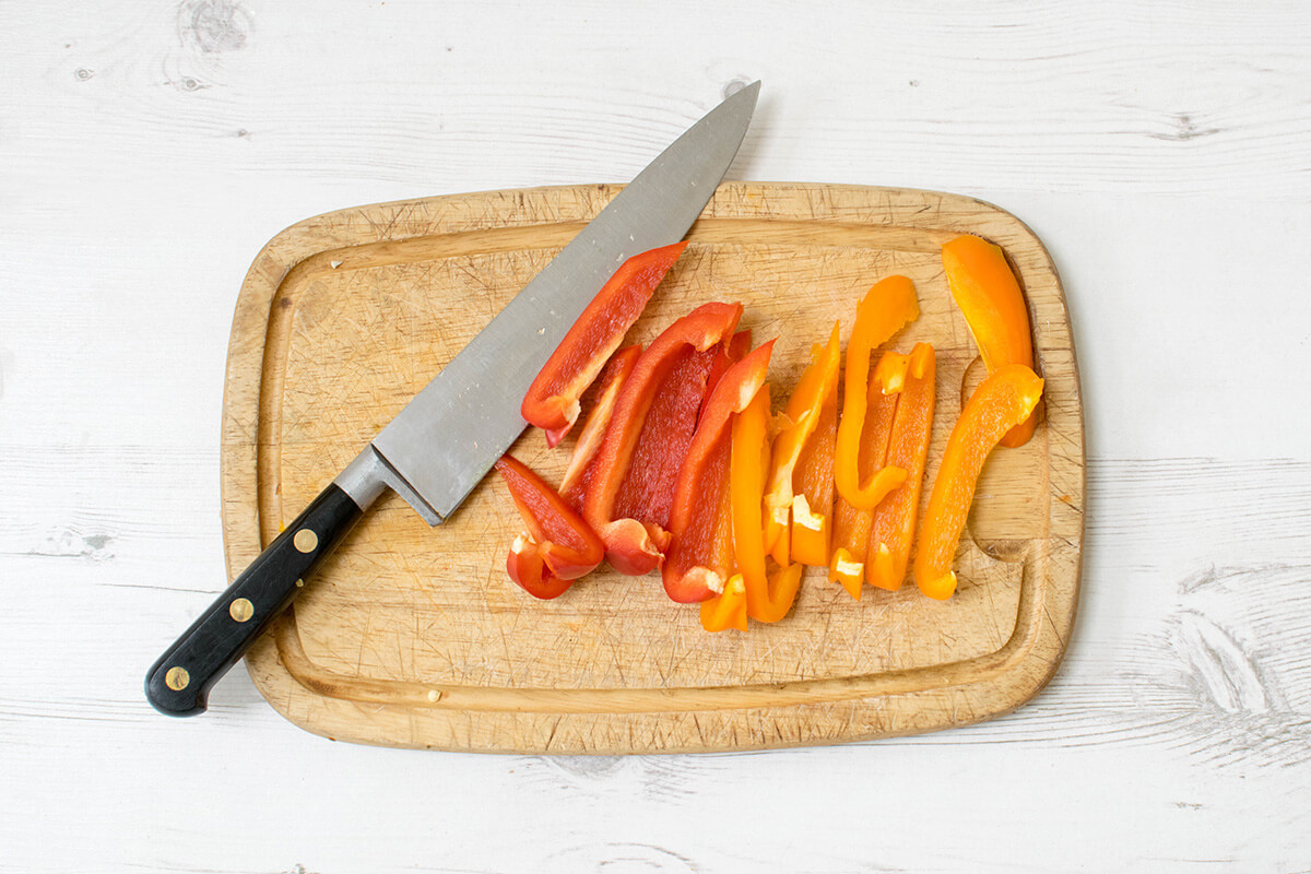 A chopping board with sliced red and orange peppers