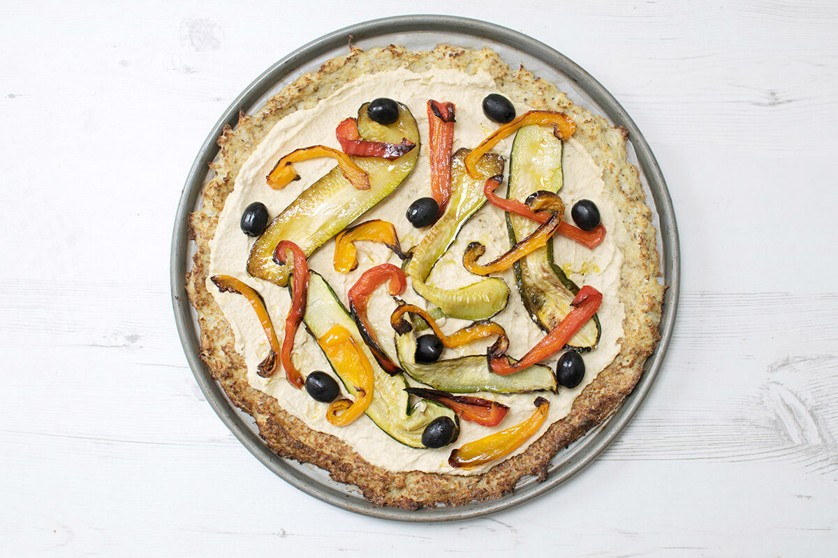 Roasted Veggie Cauliflower Pizza topped with hummus, peppers, courgette and olives